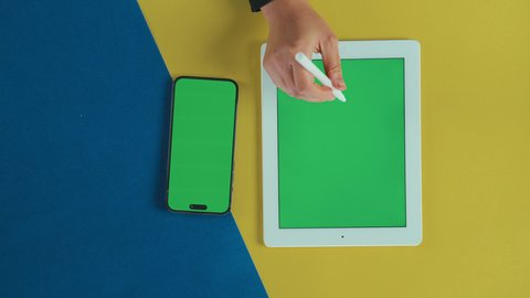 النقر على الجهاز بواسطة القلم, عرض شاشة خضراء فارغة على الأجهزة التقنية، استخدام التكنولوجيا الحديثة في انجاز المهام عن بعد، تصوير علوي عامودي ليد امرأة عربية خليجية سعودية ترتدي العباءة السوداء تستخدم تابلت و جوال, كروما