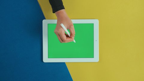 Drawing a check mark on the tablet, using technology and modern techniques, the concept of electronic correction online, an overhead vertical shot of the hand of an Arab Gulf Saudi woman wearing a black abaya using a tablet with a blank green screen, chroma.