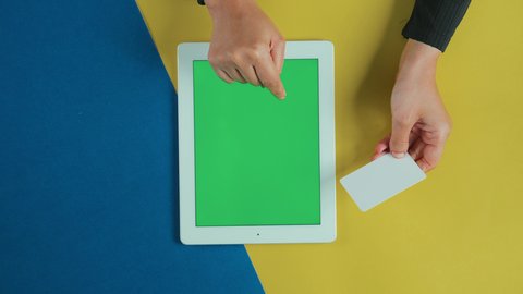 مفهوم التسوق الالكتروني الآمن، إمكانية تسديد الفواتير بالبطاقة الالكترونية، الشراء والدفع عن بعد، تصوير علوي عامودي ليد امرأة عربية خليجية سعودية ترتدي العباءة السوداء تستخدم جهاز تابلت بشاشة خضراء فارغة و تحمل بطاقة بيضاء, كروما