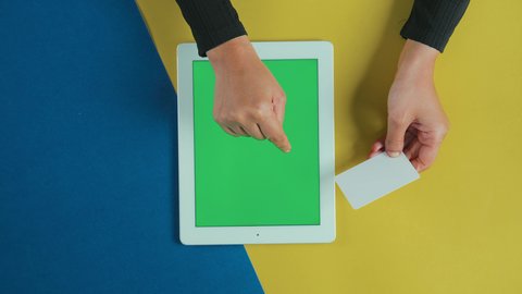 الشراء والدفع عن طريق بطاقات الصراف الإئتمانية، سهولة تسديد الفواتير عبر الحساب البنكي، تصوير علوي عامودي ليد امرأة عربية خليجية سعودية ترتدي العباءة السوداء تستخدم جهاز تابلت بشاشة خضراء فارغة و تحمل بطاقة بيضاء, مفهوم التسوق الالكتروني الآمن, كروما