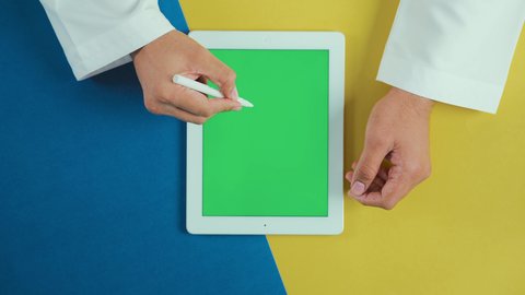 تسجيل الأفكار والمعلومات بطرق حديثة, استخدام التكنولوجيا و التقنيات المتطورة، مفهوم إدارة المشاريع وانجاز المهام عن بعد، تصوير علوي عامودي ليد رجل عربي سعودي خليجي يرتدي الثوب التقليدي و يستخدم جهاز تابلت بشاشة خضراء فارغة مع القلم الخاص به، تصفح مواقع و وسائل التواصل الاجتماعي, كروما