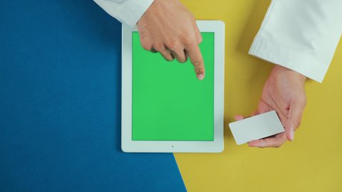 طرق الشراء الحديثة, استخدام بطاقات الائتمان البنكية, استخدام الوسائل والتقنيات الحديثة المتطورة، تصوير علوي عامودي ليد رجل عربي سعودي خليجي يرتدي الثوب التقليدي و يستخدم جهاز تابلت بشاشة خضراء فارغة و يحمل بطاقة بيضاء, كروما