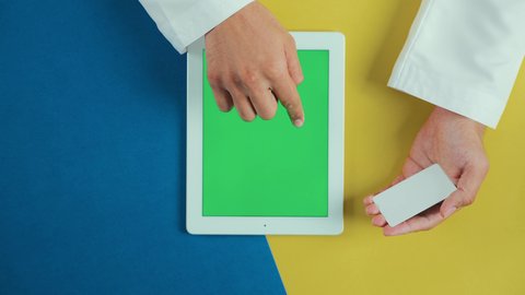 تسهيل عمليات الشراء والبيع، إمكانية تسديد الفواتير عن طريق البطاقات الالكترونية، استخدام الوسائل والتقنيات الحديثة المتطورة، تصوير علوي عامودي ليد رجل عربي سعودي خليجي يرتدي الثوب التقليدي و يستخدم جهاز تابلت بشاشة خضراء فارغة و يحمل بطاقة الائتمان, كروما