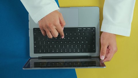 Electronic evolution and technological growth, using a laptop to accomplish tasks professionally, integrating technology and tech into practical life, following social media, holding meetings online, an overhead vertical shot of the hand of an Arab Saudi Gulf man wearing traditional attire and using a laptop.