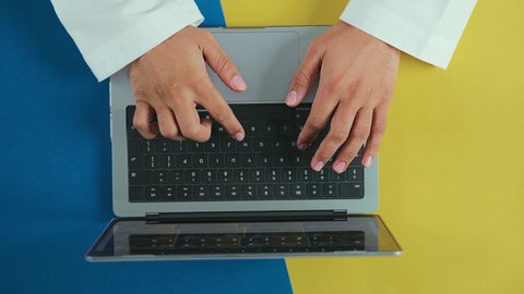 Completing the required tasks via laptop, integrating technology and tech into practical life, monitoring social media, holding meetings online, an overhead vertical shot of the hand of an Arab Saudi Gulf man wearing traditional attire and using a laptop.