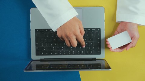 إمكانية تسديد الفواتير بالبطاقة الالكترونية، التسوق الالكتروني عبر الحاسوب المحمول، الشراء والدفع عن بعد، تصوير علوي عامودي ليدين رجل عربي سعودي خليجي يرتدي الثوب التقليدي و يقوم باستخدام بطاقة الإئتمان و اللابتوب، تطور التكنولوجيا والأجهزة التقنية