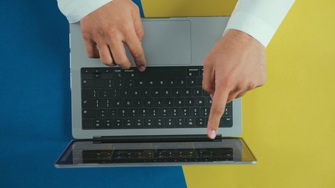 Managing and organizing business affairs via laptop, using a portable computer to accomplish tasks professionally, integrating technology and tech into practical life, monitoring social media, holding meetings online, overhead vertical shot of the hand of an Arab Saudi Gulf man wearing traditional attire.
