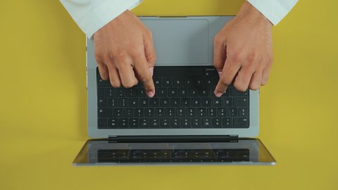 Using a laptop to accomplish tasks professionally, integrating technology and tech into practical life, following social media, holding meetings online, an overhead vertical shot of the hand of an Arab Saudi Gulf man wearing traditional attire and using a laptop.