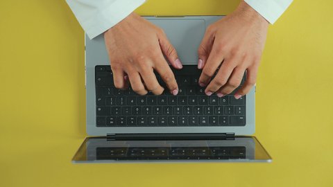 Integrating technology and tech into practical life, following social media, holding meetings online, using a laptop to accomplish work, an overhead vertical shot of the hand of an Arab Saudi Gulf man wearing traditional attire and using a laptop.