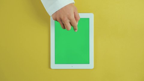 Tapping with the index finger on the tablet screen, using modern technology and techniques, the concept of project management and completing tasks remotely, an overhead vertical shot of the hand of an Arab Saudi Gulf man wearing traditional attire and using a tablet, browsing social media sites, chroma.