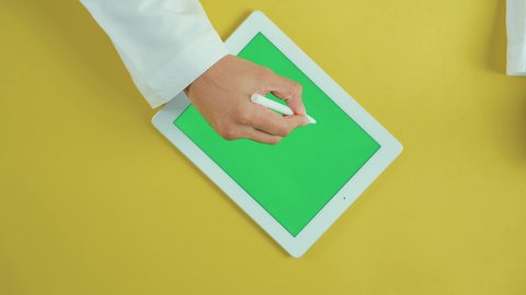 Using a special pen to press on the tablet, using modern technology and techniques, the concept of project management and completing tasks remotely, an overhead vertical shot of the hand of an Arab Saudi Gulf man wearing traditional attire and using a tablet with a blank green screen, browsing social media sites, chroma.