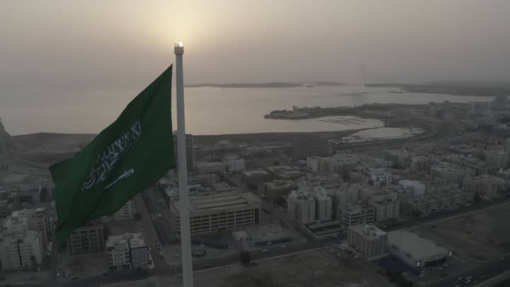 Jeddah's waterfront, the green flag of unity waving in the sky, the squares, streets, and famous landmarks of Jeddah, drone footage of King Abdullah Financial Street in the city of Jeddah in the Kingdom of Saudi Arabia at sunset, car traffic, towers and residential buildings, the beauty of the city of Jeddah.