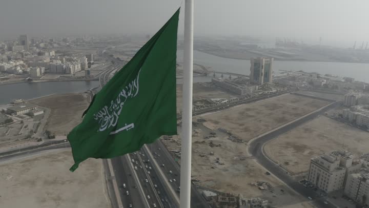 راية التوحيد الخضراء ترفر في السماء، كورنيش جدة البحري، ميدان وشوارع ومعالم جدة المشهورة، تصوير درون لطريق الملك عبد الله المالي في مدينة جدة في المملكة العربية السعودية في وقت الغروب، حركة مرور السيارات، الابراج والمباني السكنية، جمال مدينة جدة