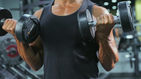 تقوية عضلات الجسم وبناؤها، القوة والتحدي والتحفيز لأسلوب حياة صحي، نشاط بدني للمحافظة على الصحة واللياقة الجسدية، رفع الأوزان الحديدية الثقيلة، تمارين رفع الأثقال، شاب عربي خليجي سعودي يرتدي الزي الرياضي يمارس التمارين الرياضية مع الدمبلز