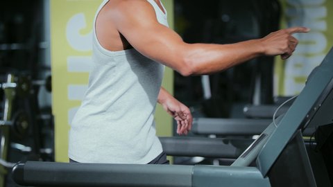 تعزيز الصحة واللياقة البدنية، استخدام الاجهزة الرياضية، القيام بالأنشطة الترفيهية الممتعة، نادي الألعاب الرياضية، ممارسة تمارين الاحماء, شاب عربي خليجي سعودي يرتدي الملابس الرياضية يقوم بالمشي على الجهاز الكهربائي