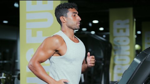 القيام بالأنشطة الترفيهية الممتعة، نادي الألعاب الرياضية، ممارسة تمارين الاحماء، المحافظة على الصحة واللياقة البدنية, شاب عربي خليجي سعودي يرتدي الملابس الرياضية يقوم بالمشي على الجهاز الكهربائي، استخدام الاجهزة الرياضية