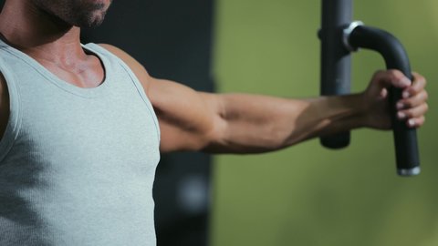 Using sports equipment, the importance of sports for building a strong body, a young Arab Gulf Saudi man wearing sportswear practicing an exercise to strengthen the chest, arms, and shoulders on the parallel bars, strengthening nerves and muscles, a healthy lifestyle.