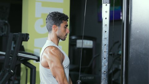 مفهوم اللياقة والرشاقة، نمط حياة صحي ومفيد، حرق الدهون وتقليل الوزن، نشاط لتقوية العضلات، استخدام الأجهزة الرياضية، شاب عربي خليجي سعودي يرتدي الزي الرياضي يقوم بممارسة تمارين الظهر على آلة السحب العلوي