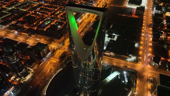 Growth, development, and urban progress, a drone shot of the famous Kingdom Tower illuminated at night, the buildings and famous commercial landmarks in the Kingdom of Saudi Arabia, the architectural engineering art in the modern and advanced style of towers and skyscrapers in the city of Riyadh.