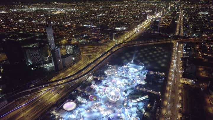 Population congestion in the capital, drone footage of the illuminated Winter Wonderland amusement park at night in Riyadh, Saudi Arabia, tourist attractions in Saudi Arabia, Riyadh Season events, entertainment and fun, towers and skyscrapers.