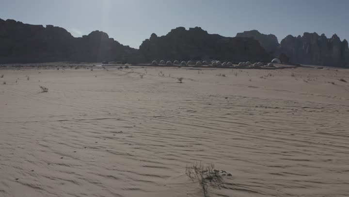 A youth camping trip in the deserts of the Kingdom of Saudi Arabia, tourist camps in the wilderness, drone photography of a group of tents amidst the sands, Bedouin life in the desert, the terrain and soft golden dunes, and thorny plants.