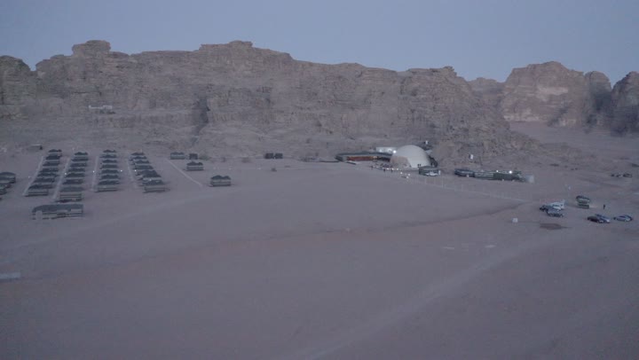 A youth camping trip in the deserts of the Kingdom of Saudi Arabia, tourist camps in the wilderness, drone photography of a group of tents amidst the sands, Bedouin life in the desert, the terrain and soft golden dunes, and thorny plants.