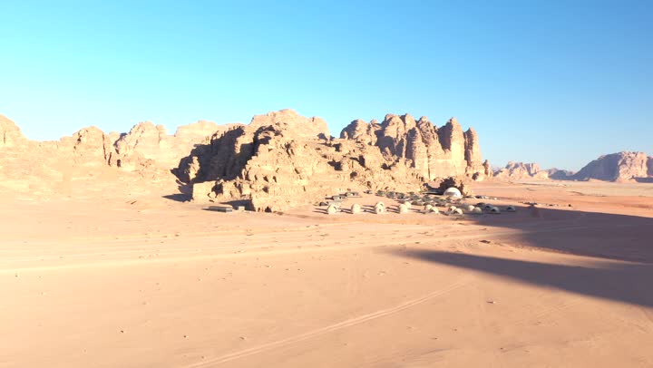 A youth camping trip in the deserts of the Kingdom of Saudi Arabia, tourist camps in the wilderness, drone photography of a group of tents amidst the sands, Bedouin life in the desert, the terrain and soft golden dunes, and thorny plants.