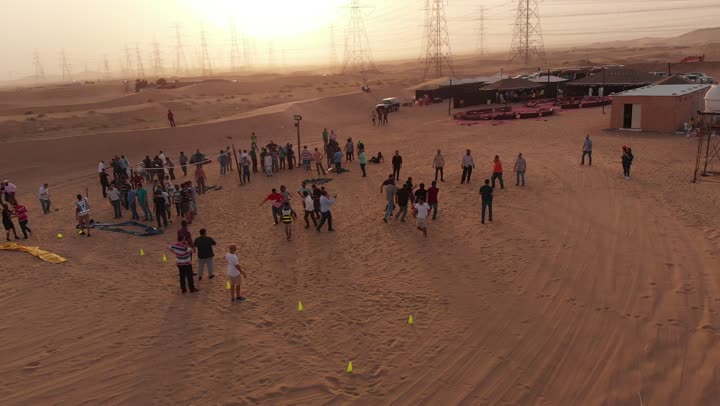 Adventure and exploration, the landscapes and soft golden sands in the desert, the soft golden dunes and natural terrain in the Kingdom of Saudi Arabia, the concept of mobility and movement, aerial drone footage of a group of Arab Saudi Gulf individuals walking somewhere in the desert.