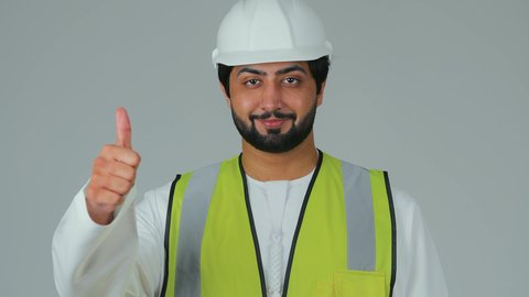 علامة الجودة والامتياز، مفهوم الإنشاءات المعمارية، بورتريه مقرب لمهندس عربي خليجي إماراتي يرتدي الكندورة والخوذة وسترة الحماية يرفع إصبع الإبهام للأعلى بإيماءات الإعجاب، المهن والوظائف الشبابية في الإمارات العربية المتحدة، خلفية بيضاء