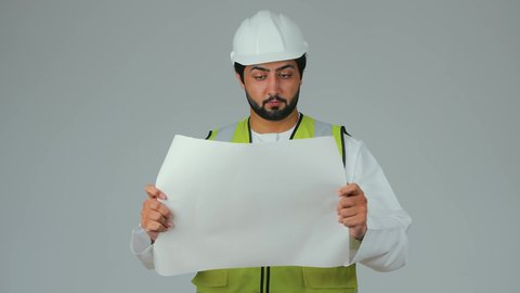 دراسة العناصر الأساسية للمخططات الهندسية، مفهوم الهندسة والانشاءات المعمارية،  بورتريه لمهندس عربي خليجي إماراتي يرتدي الكندورة والسترة الخاصة بالعمل يمسك المخطط ينظر إليه بايماءات التركيز والتمعن، مهنة ووظيفة للشباب في الامارات العربية، العمل في القطاع الهندسي، خلفية بيضاء