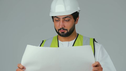 الاطلاع على قواعد المخطط الإنشائي، مفهوم الهندسة والانشاءات المعمارية،  بورتريه لمهندس عربي خليجي إماراتي يرتدي الكندورة والسترة الخاصة بالعمل يمسك المخطط ينظر إليه بايماءات التركيز والتمعن، مهنة ووظيفة للشباب في الامارات العربية، العمل في القطاع الهندسي، خلفية بيضاء