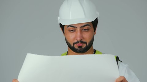 Study of the fundamentals of structural planning, the concept of engineering and architectural constructions, a close-up portrait of an Emirati Gulf Arab engineer wearing a kandura and work jacket holding the plan and looking at it with gestures of focus and contemplation, a profession and job for youth in the United Arab Emirates, working in the engineering sector, white background.