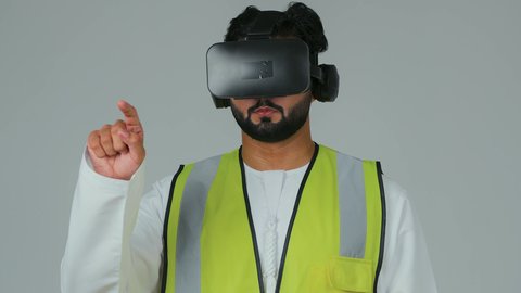 التفاعل مع محاكاة الهندسة الرقمية، تجسيد ومشاهدة المشاريع الهندسية بالاعتماد على التكنولوجيا، بورتريه لمهندس عربي خليجي إماراتي يرتدي الكندورة والسترة الخاصة بالعمل ونظارة الواقع الافتراضي يرفع يديه للمس عناصر هولوجرامية، خلفية بيضاء