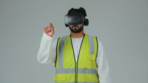 تجسيد ومشاهدة المشاريع الهندسية بالاعتماد على التكنولوجيا، الاندماج مع الهندسة الافتراضية، بورتريه لمهندس عربي خليجي إماراتي يرتدي الكندورة والسترة الخاصة بالعمل ونظارة الواقع الافتراضي يرفع يديه للمس عناصر هولوجرامية، خلفية بيضاء