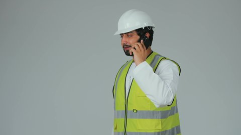 Remote work follow-up, use of modern technical devices, youth professions and jobs, work in the engineering sector, a portrait of an Emirati Gulf Arab engineer wearing a kandura, helmet, and safety vest holding a mobile phone making a phone call, integrating advanced technology with engineering, white background.