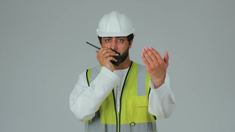 تنظيم سير العمل عبر إصدار الأوامر، متابعة سير الاعمال، العمل في القطاع الهندسي، الإشراف على المشاريع، بورتريه لمهندس عربي خليجي إماراتي يرتدي الكندورة والخوذة وسترة الحماية يقوم باستخدام جهاز الاتصال اللاسلكي، مهن وظائف هندسية، خلفية بيضاء