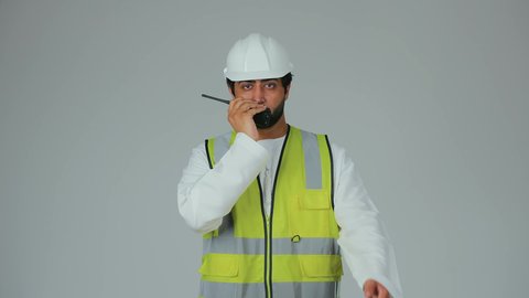 إعطاء توجيهات محددة للمهام اليومية، متابعة سير الاعمال، العمل في القطاع الهندسي، الإشراف على المشاريع، بورتريه لمهندس عربي خليجي إماراتي يرتدي الكندورة والخوذة وسترة الحماية يقوم باستخدام جهاز الاتصال اللاسلكي، مهن وظائف هندسية، خلفية بيضاء