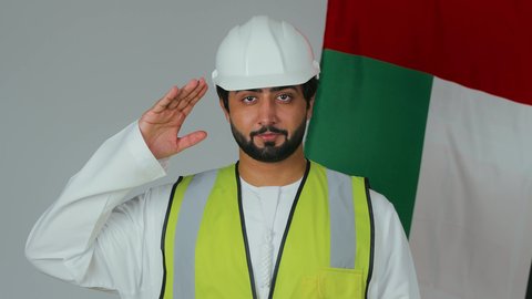 إحياء ذكرى إستقلال الإمارات، الوقوف بإنضباط وإلقاء التحية للوطن والعلم،بورتريه لمهندس عربي خليجي إماراتي يرتدي الكندورة والخوذة وسترة الحماية ينظر بتعابير الفخر، الإحتفال بالعيد الوطني الإماراتي، علم دولة الإمارات العربية المتحدة، خلفية بيضاء