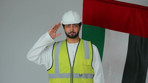 الوقوف بإنضباط وإلقاء التحية للوطن والعلم،بورتريه لمهندس عربي خليجي إماراتي يرتدي الكندورة والخوذة وسترة الحماية ينظر بتعابير الفخر، إحياء ذكرى إستقلال الإمارات، الإحتفال بالعيد الوطني الإماراتي، علم دولة الإمارات العربية المتحدة، خلفية بيضاء