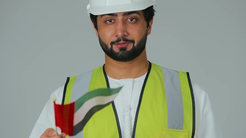 ذكرى استقلال الإمارات 1971، هوية اليوم الوطني الاماراتي 2 ديسمبر، بورتريه لمهندس عربي خليجي إماراتي يرتدي الكندورة والخوذة وسترة الحماية يحمل علم الإمارات بتعابير المحبة والفخر، الحب والانتماء للوطن، الاحتفال بالأعياد والمناسبات الوطنية، خلفية بيضاء