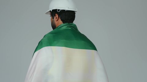 Love and connection to the homeland is the identity of the UAE National Day on December 2nd, looking at the camera with gestures of pride and confidence, commemorating the independence of the UAE in 1971, a portrait of an Arab Gulf Emirati engineer wearing the kandura, helmet, and safety vest, carrying the flag of the United Arab Emirates on his back, with a white background.