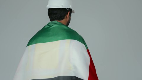النظر الى الكاميرا بايماءات الاعتزاز والثقة، الحب والانتماء للوطن، احياء ذكرى استقلال الإمارات 1971،  بورتريه لمهندس عربي خليجي إماراتي يرتدي الكندورة والخوذة وسترة الحماية يحمل علم دولة الإمارات المتحدة على ظهره، هوية اليوم الوطني الاماراتي 2 ديسمبر، خلفية بيضاء