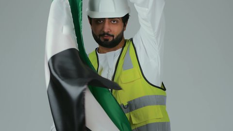 الحب والانتماء للوطن، احياء ذكرى استقلال الإمارات 1971،  بورتريه لمهندس عربي خليجي إماراتي يرتدي الكندورة والخوذة وسترة الحماية يحمل علم دولة الإمارات المتحدة على ظهره، النظر الى الكاميرا بايماءات الاعتزاز والثقة، هوية اليوم الوطني الاماراتي 2 ديسمبر، خلفية بيضاء