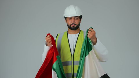 الاعتزاز بالانتماء للوطن، يوم العلم الإماراتي 3 نوفمبر، ذكرى قيام الاتحاد 2 ديسمبر 1971، بورتريه لمهندس عربي خليجي إماراتي يرتدي الكندورة والخوذة وسترة الحماية يقبل علم دولة الإمارات المتحدة، العمل في القطاع الهندسي، خلفية بيضاء