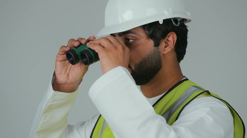 البحث عن الفرص المستقبلية، توسيع زاوية النظر، الإشراف على المشاريع الهندسية، القطاع الهندسي في الإمارات، بورتريه لمهندس عربي خليجي إماراتي يرتدي الكندورة والخوذة وسترة الحماية ينظر عبر منظار ثنائي العينين، خلفية بيضاء