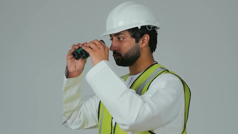 وضع خطط مستقبلية، توسيع زاوية النظر، الإشراف على المشاريع الهندسية، القطاع الهندسي في الإمارات، بورتريه لمهندس عربي خليجي إماراتي يرتدي الكندورة والخوذة وسترة الحماية ينظر عبر منظار ثنائي العينين، خلفية بيضاء