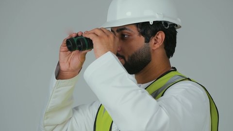 توسيع نطاق النظر، الإشراف على المشاريع الهندسية، القطاع الهندسي في الإمارات، بورتريه لمهندس عربي خليجي إماراتي يرتدي الكندورة والخوذة وسترة الحماية ينظر عبر منظار ثنائي العينين، التخطيط والبحث للمستقبل، خلفية بيضاء
