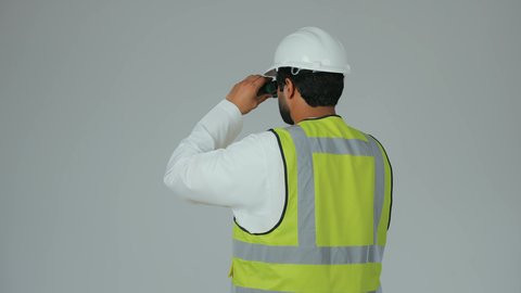 توسيع مجال الرؤية، الإشراف على المشاريع الهندسية، القطاع الهندسي في الإمارات، بورتريه من الخلف لمهندس عربي خليجي إماراتي يرتدي الكندورة والخوذة وسترة الحماية ينظر عبر منظار ثنائي العينين، التخطيط والبحث للمستقبل، خلفية بيضاء