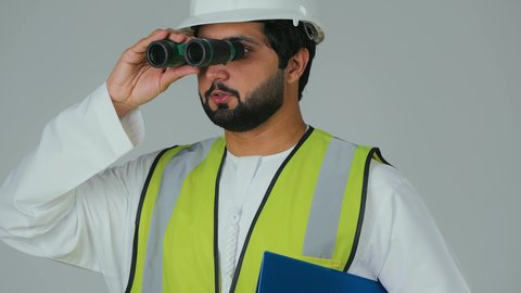 Planning and research for the future, expanding the field of vision, supervising engineering projects, the engineering sector in the UAE, a close-up portrait of an Arab Gulf Emirati engineer wearing a kandura, helmet, and safety vest looking through binoculars while holding a blue work file in his hand, white background.
