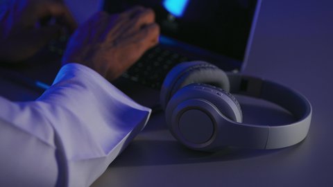 Typing on the keyboard, benefiting from modern technology, the concept of listening and hearing, a close-up shot of the hand of a Saudi Gulf Arab man using a laptop with a headset next to him.